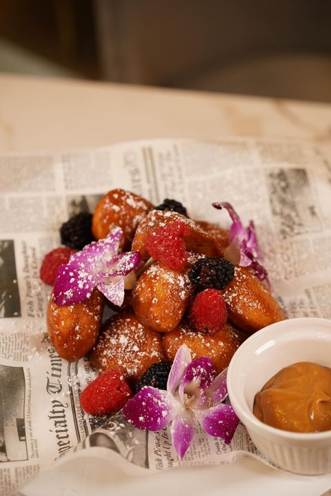 Homemade doughnuts dusted with powdered sugar, with berries, orchids and dulce de leche sauce